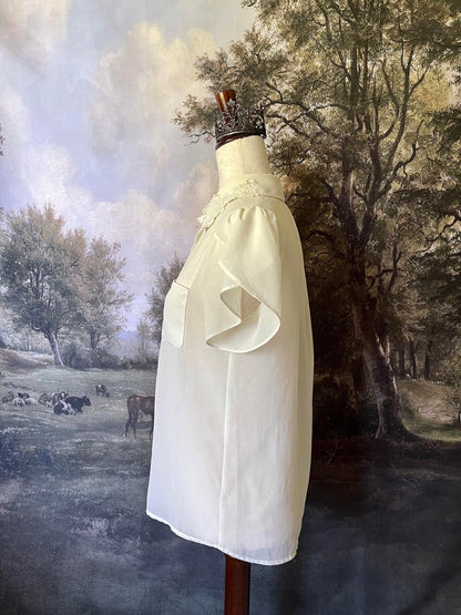 A historically inspired Vintage era Chiffon Button-up Blouse with Short Flutter Sleeves and a lace collar is pictured on a mannequin in front of an art history backdrop.