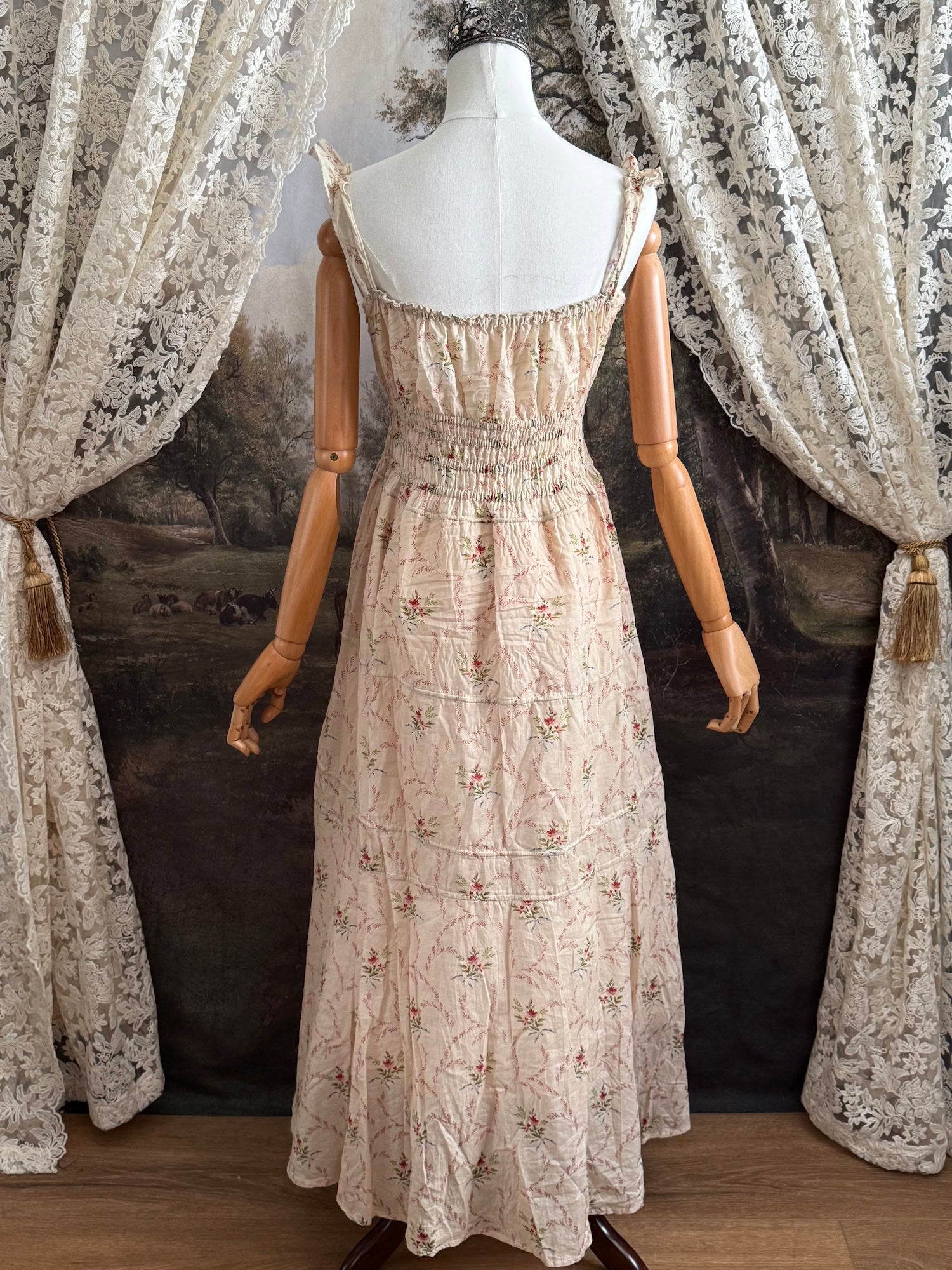 A historically inspired vintage bouquet print floral sleeveless regency rococo style maxi dress with tiered skirt and shirred bodice on a mannequin in front of an art history backdrop