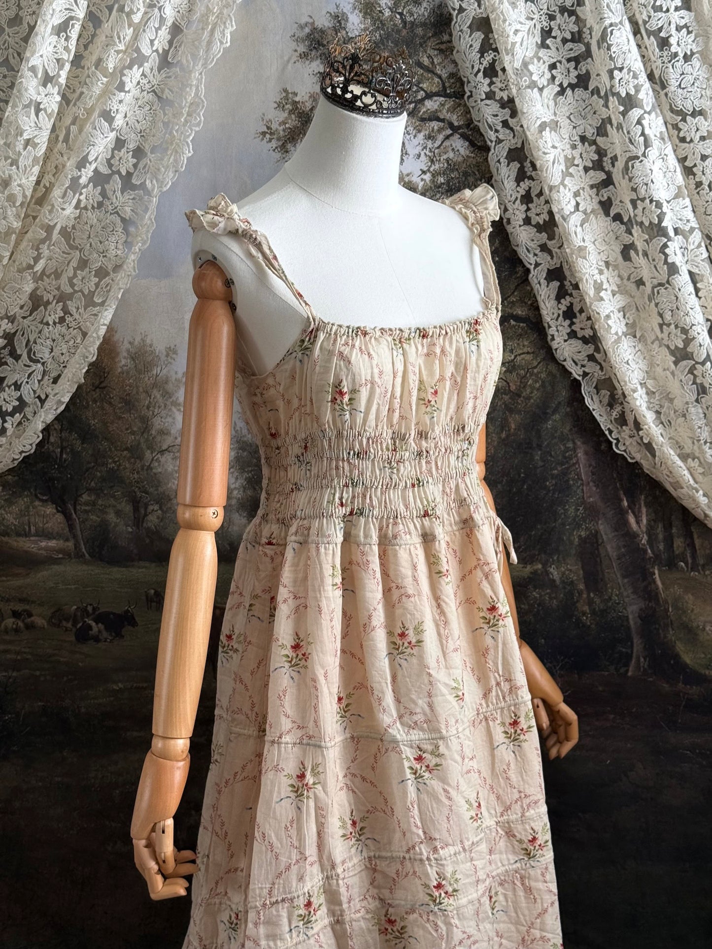 A historically inspired vintage bouquet print floral sleeveless regency rococo style maxi dress with tiered skirt and shirred bodice on a mannequin in front of an art history backdrop