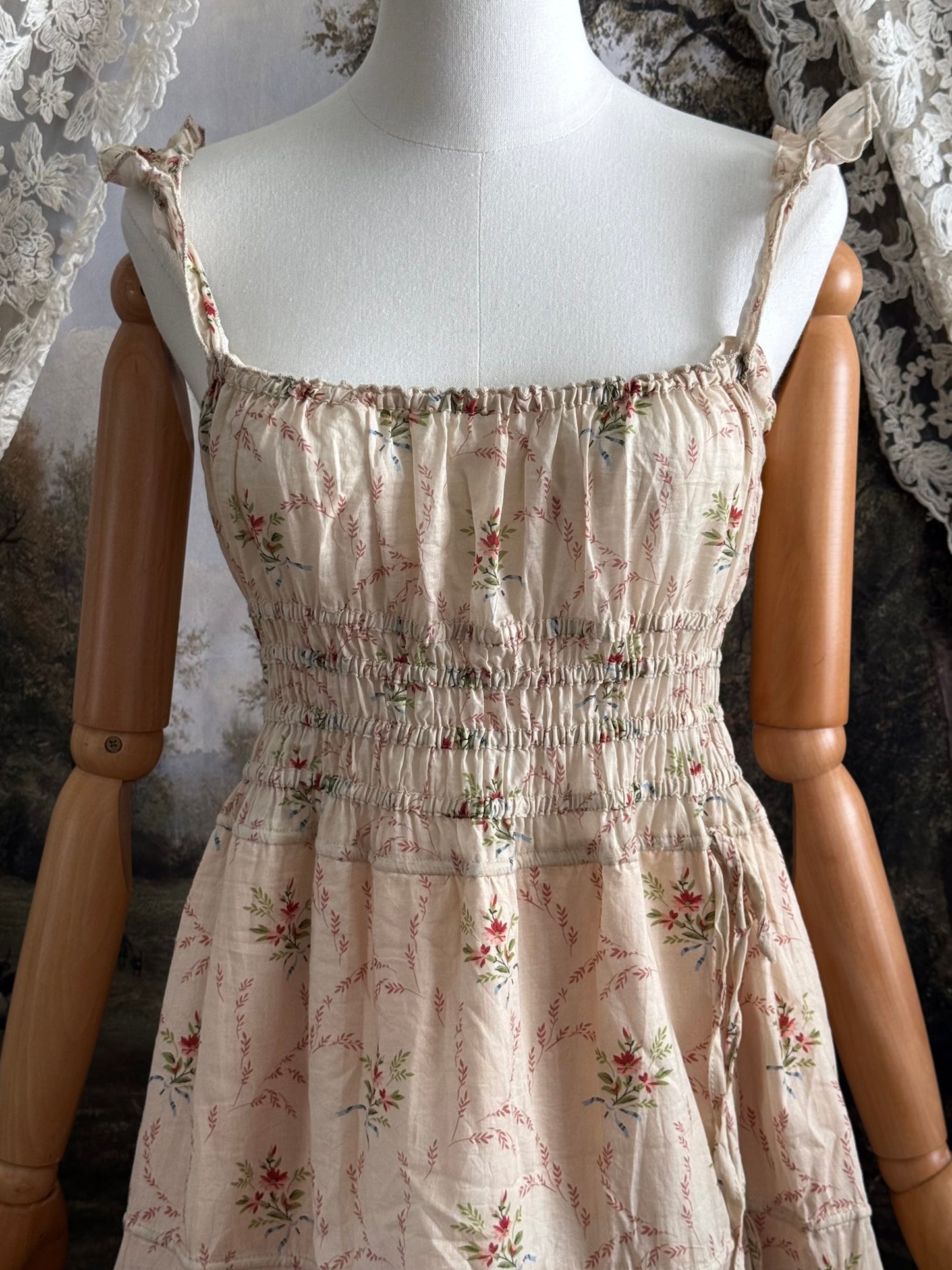 A historically inspired vintage bouquet print floral sleeveless regency rococo style maxi dress with tiered skirt and shirred bodice on a mannequin in front of an art history backdrop