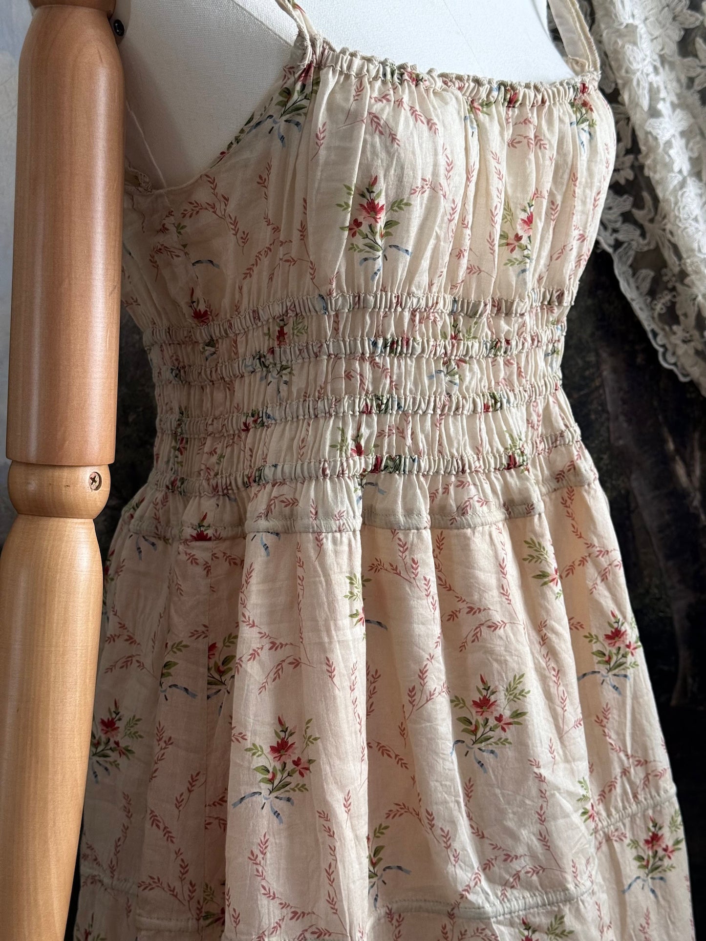 A historically inspired vintage bouquet print floral sleeveless regency rococo style maxi dress with tiered skirt and shirred bodice on a mannequin in front of an art history backdrop
