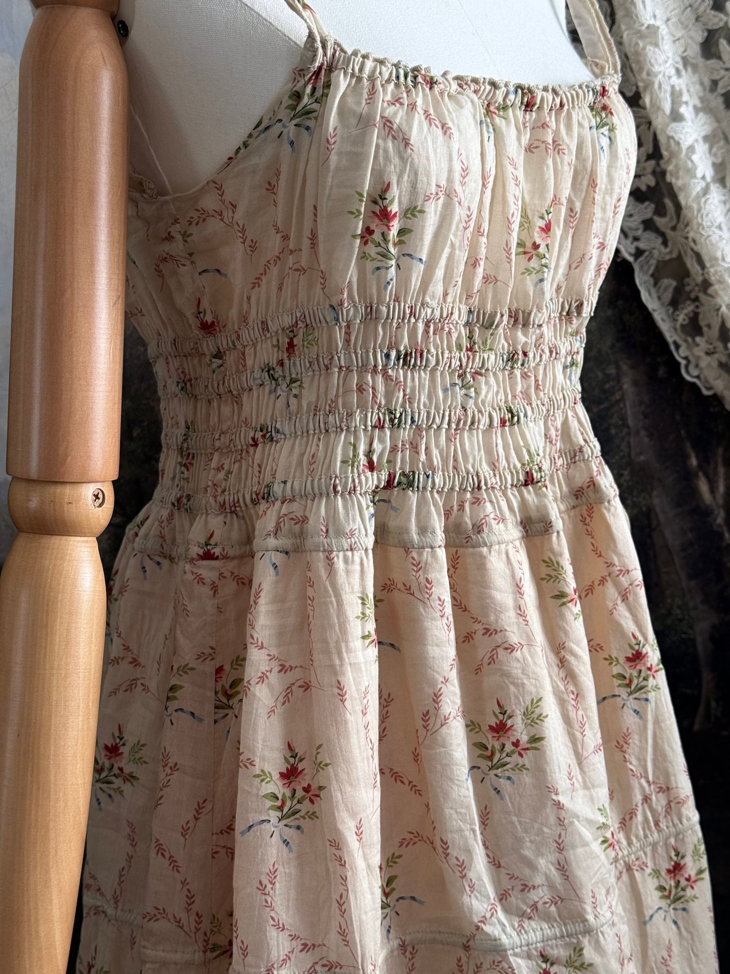 A historically inspired vintage bouquet print floral sleeveless regency rococo style maxi dress with tiered skirt and shirred bodice on a mannequin in front of an art history backdrop