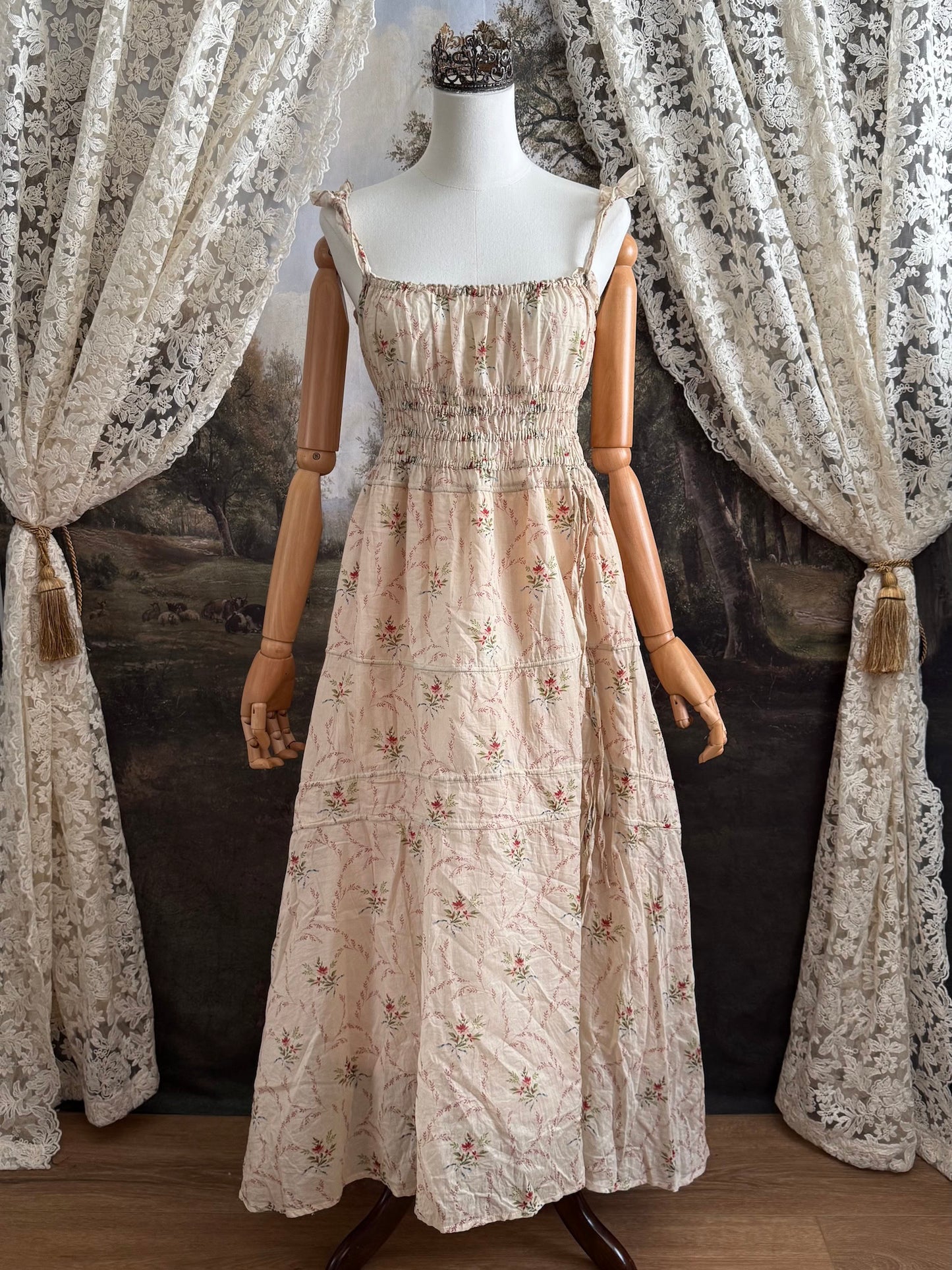 A historically inspired vintage bouquet print floral sleeveless regency rococo style maxi dress with tiered skirt and shirred bodice on a mannequin in front of an art history backdrop