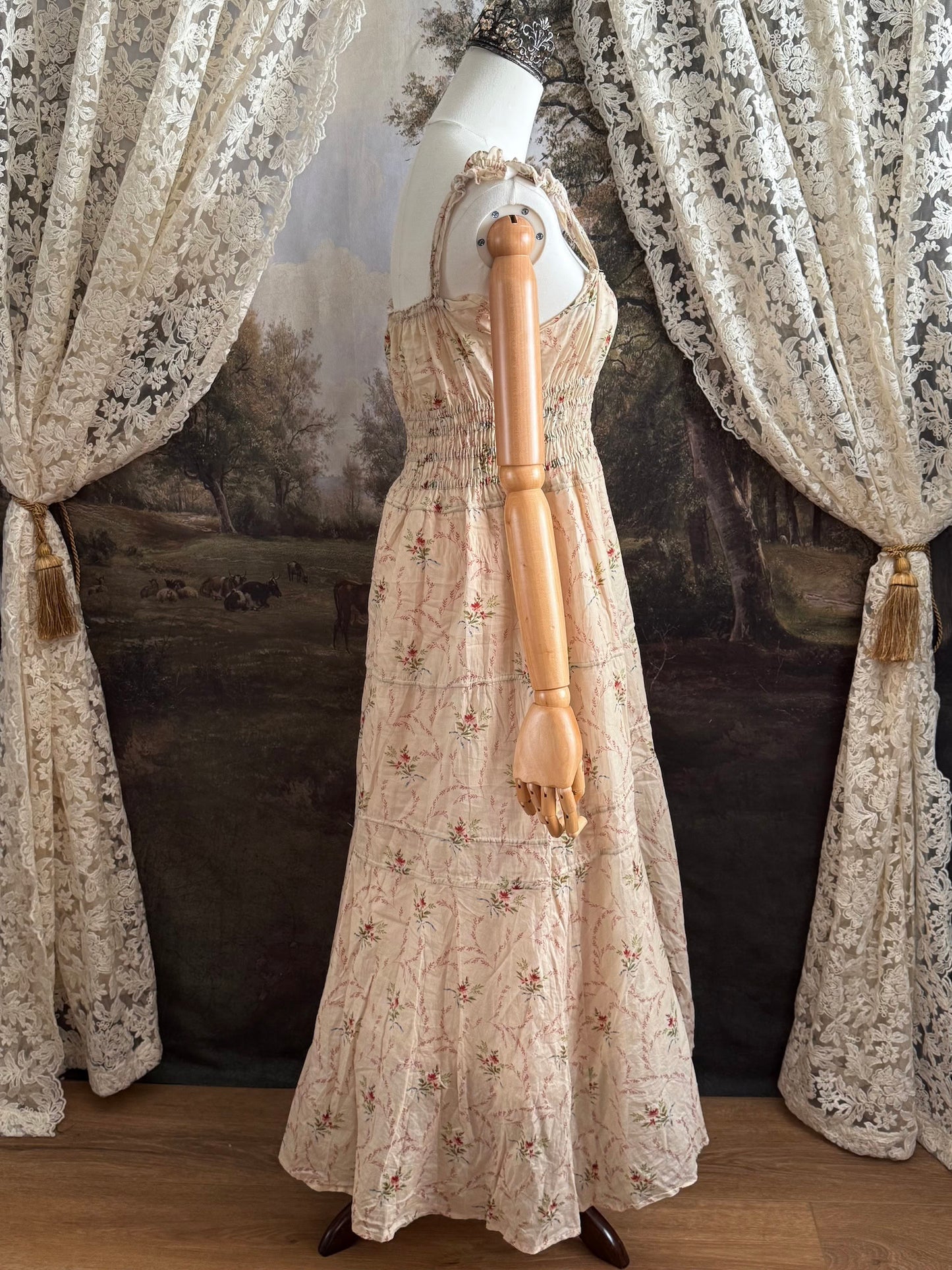 A historically inspired vintage bouquet print floral sleeveless regency rococo style maxi dress with tiered skirt and shirred bodice on a mannequin in front of an art history backdrop