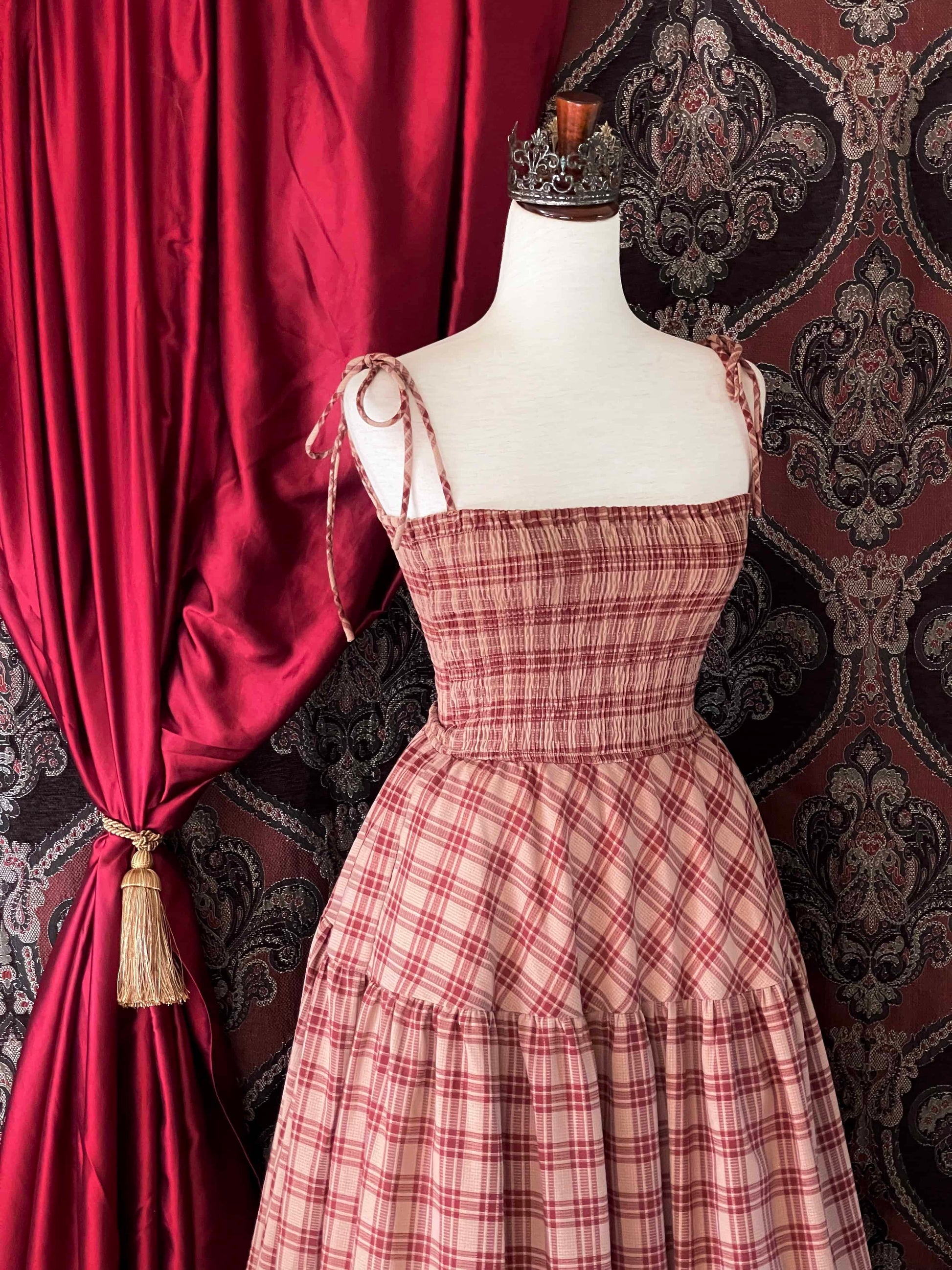 An early medieval era, Anglo Saxon, historically inspired rust and burgundy tartan plaid smocked maxi dress with tiered skirt pictured on a mannequin.