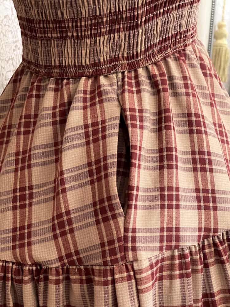 Pocket detail on an early medieval era, Anglo Saxon, historically inspired rust and burgundy tartan plaid smocked maxi dress with tiered skirt.