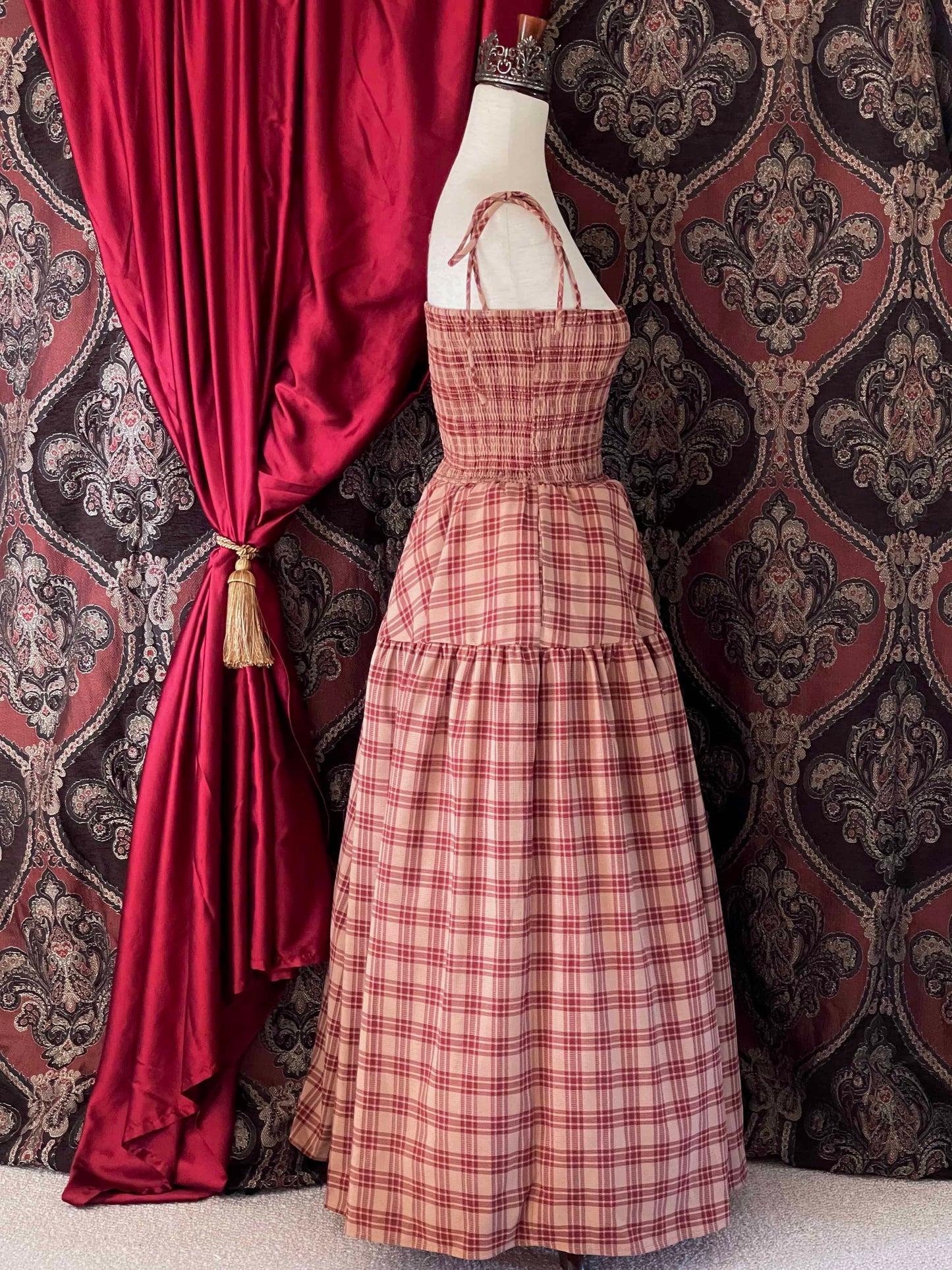 An early medieval era, Anglo Saxon, historically inspired rust and burgundy tartan plaid smocked maxi dress with tiered skirt pictured on a mannequin.
