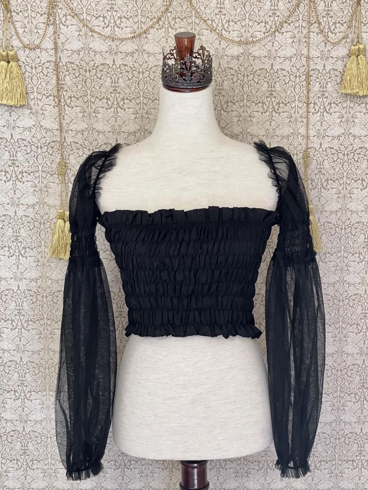 A historically inspired gothic black smocked blouse with mesh juliet sleeves is pictured on a mannequin in front of a William Morris wallpaper.