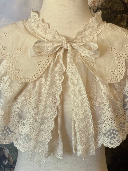 A Historically inspired edwardian victorian regency and rococo style lace capelet shawl in ivory with bow and floral embroidered details.