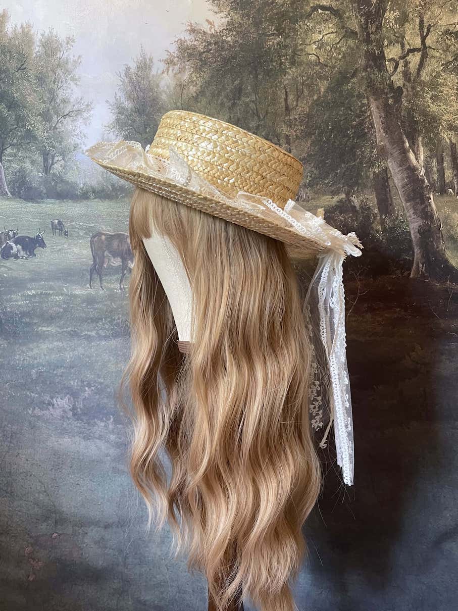 A Historically Inspired straw boater hat on a mannequin. Decorated with cotton crochet floral lace bows.