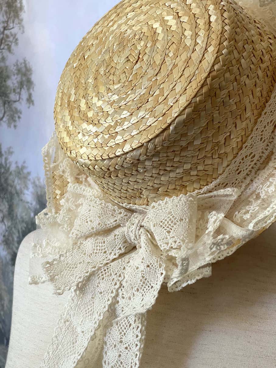 A Historically Inspired straw boater hat on a mannequin. Decorated with cotton crochet floral lace bows.