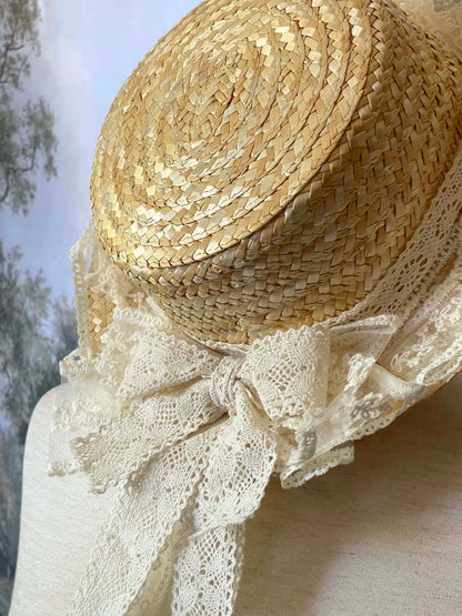A Historically Inspired straw boater hat on a mannequin. Decorated with cotton crochet floral lace bows.