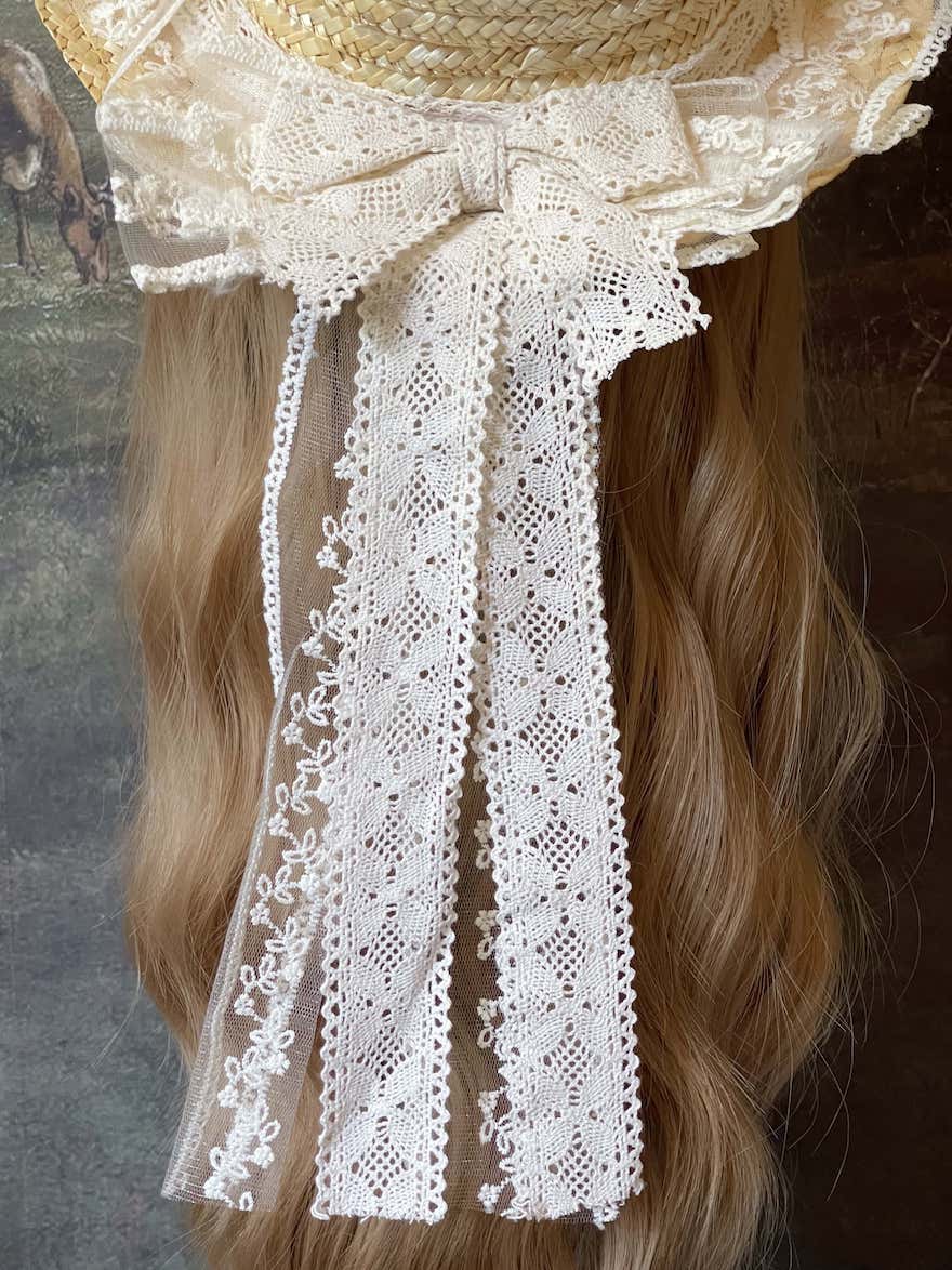 A Historically Inspired straw boater hat on a mannequin. Decorated with cotton crochet floral lace bows.