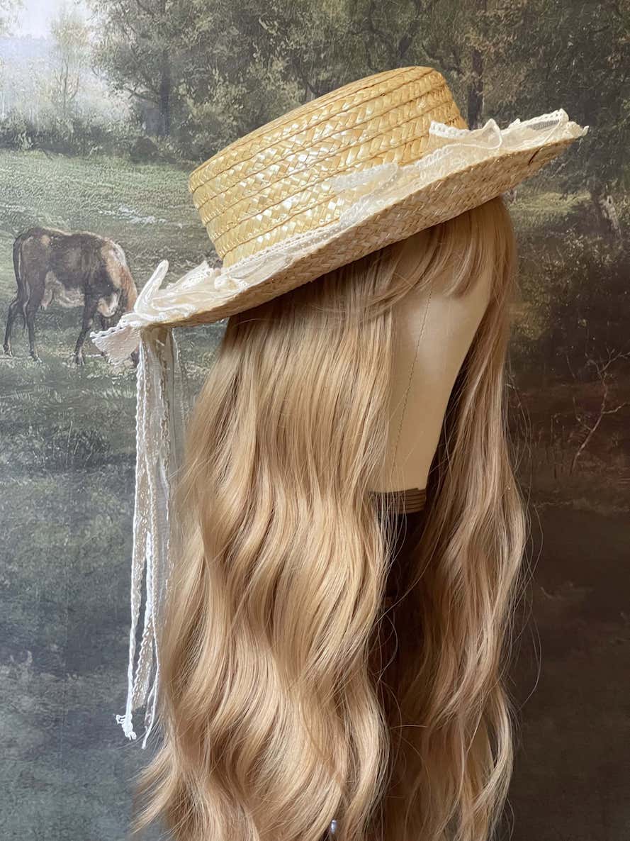 A Historically Inspired straw boater hat on a mannequin. Decorated with cotton crochet floral lace bows.
