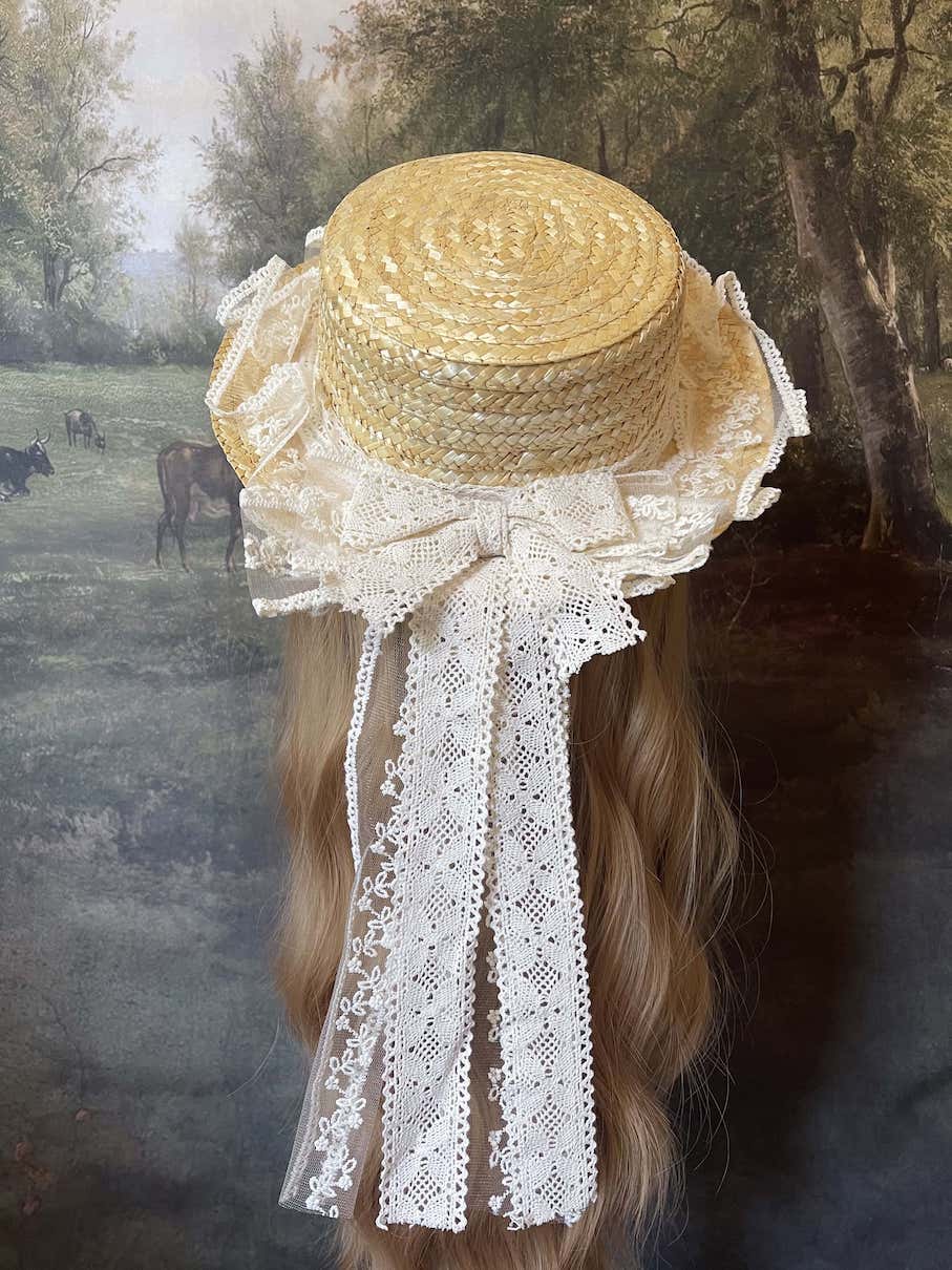 A Historically Inspired straw boater hat on a mannequin. Decorated with cotton crochet floral lace bows.