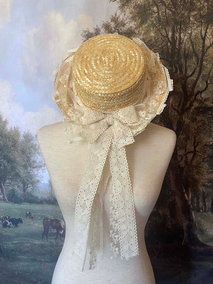 A Historically Inspired straw boater hat on a mannequin. Decorated with cotton crochet floral lace bows.