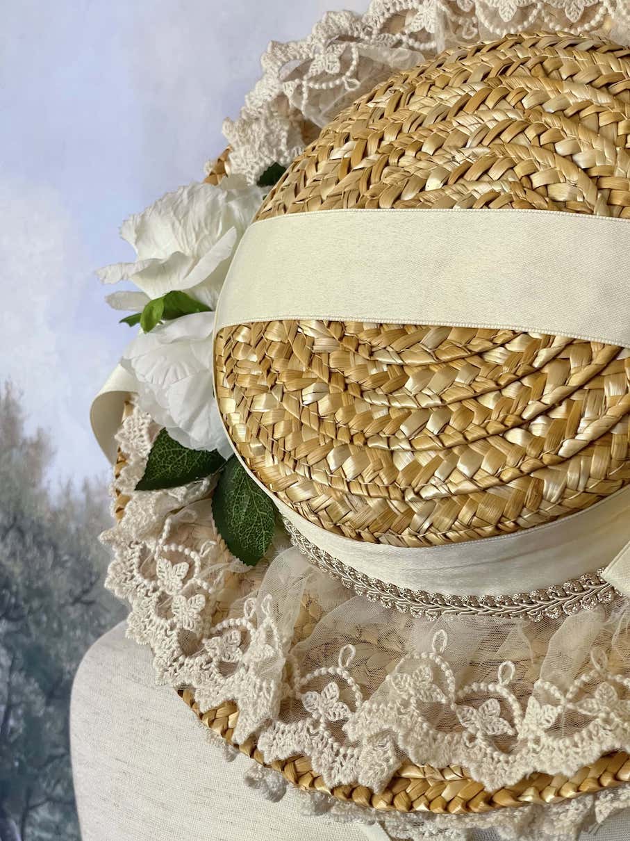 A historically inspired straw bonnet style hat with floral decorations, bow embellishments, ribbons, and lace.  Reminiscent of regency, rococo, victorian, and edwardian eras.