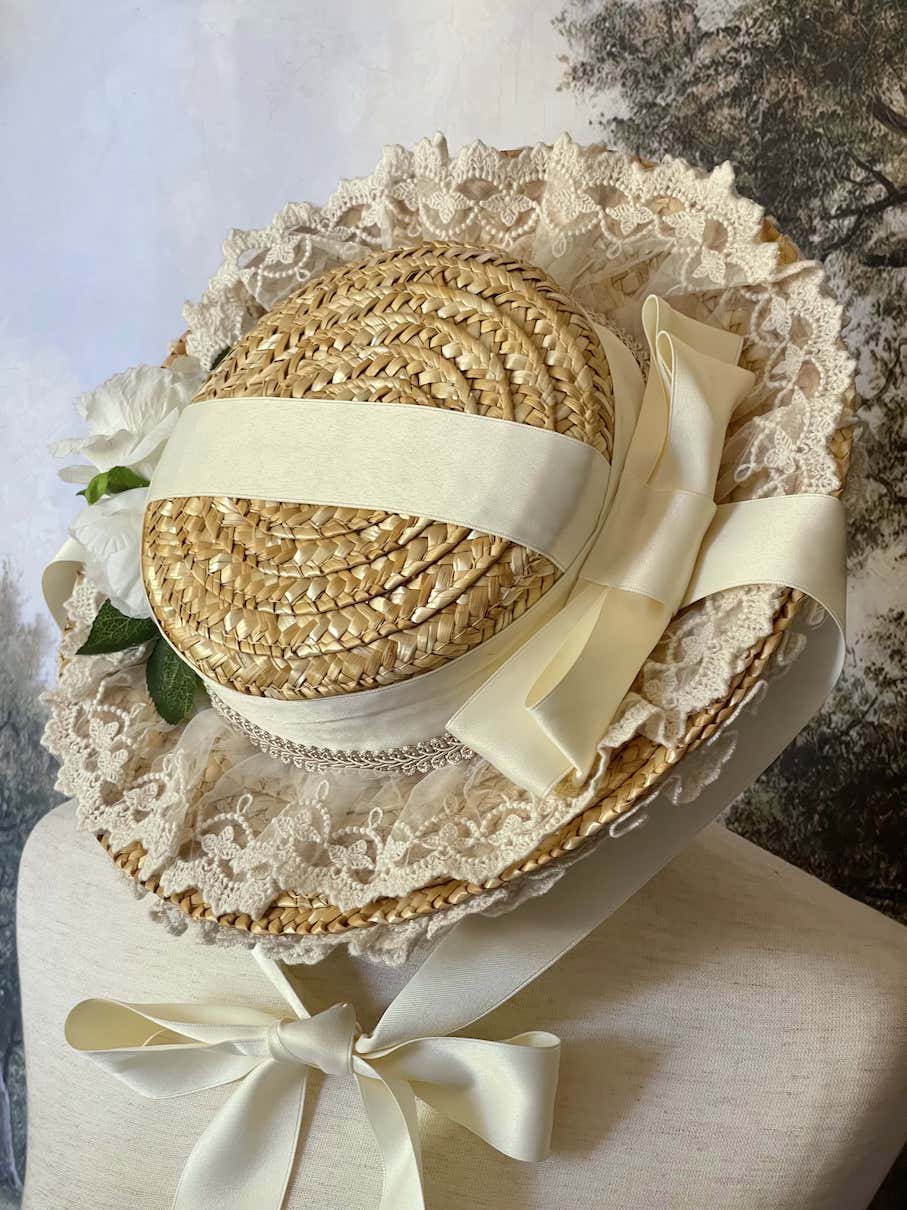 A historically inspired straw bonnet style hat with floral decorations, bow embellishments, ribbons, and lace.  Reminiscent of regency, rococo, victorian, and edwardian eras.