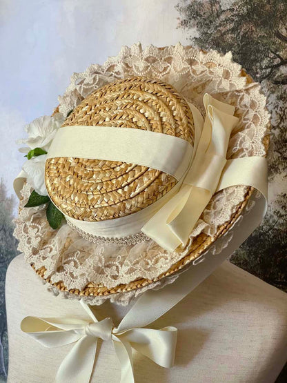 A historically inspired straw bonnet style hat with floral decorations, bow embellishments, ribbons, and lace.  Reminiscent of regency, rococo, victorian, and edwardian eras.