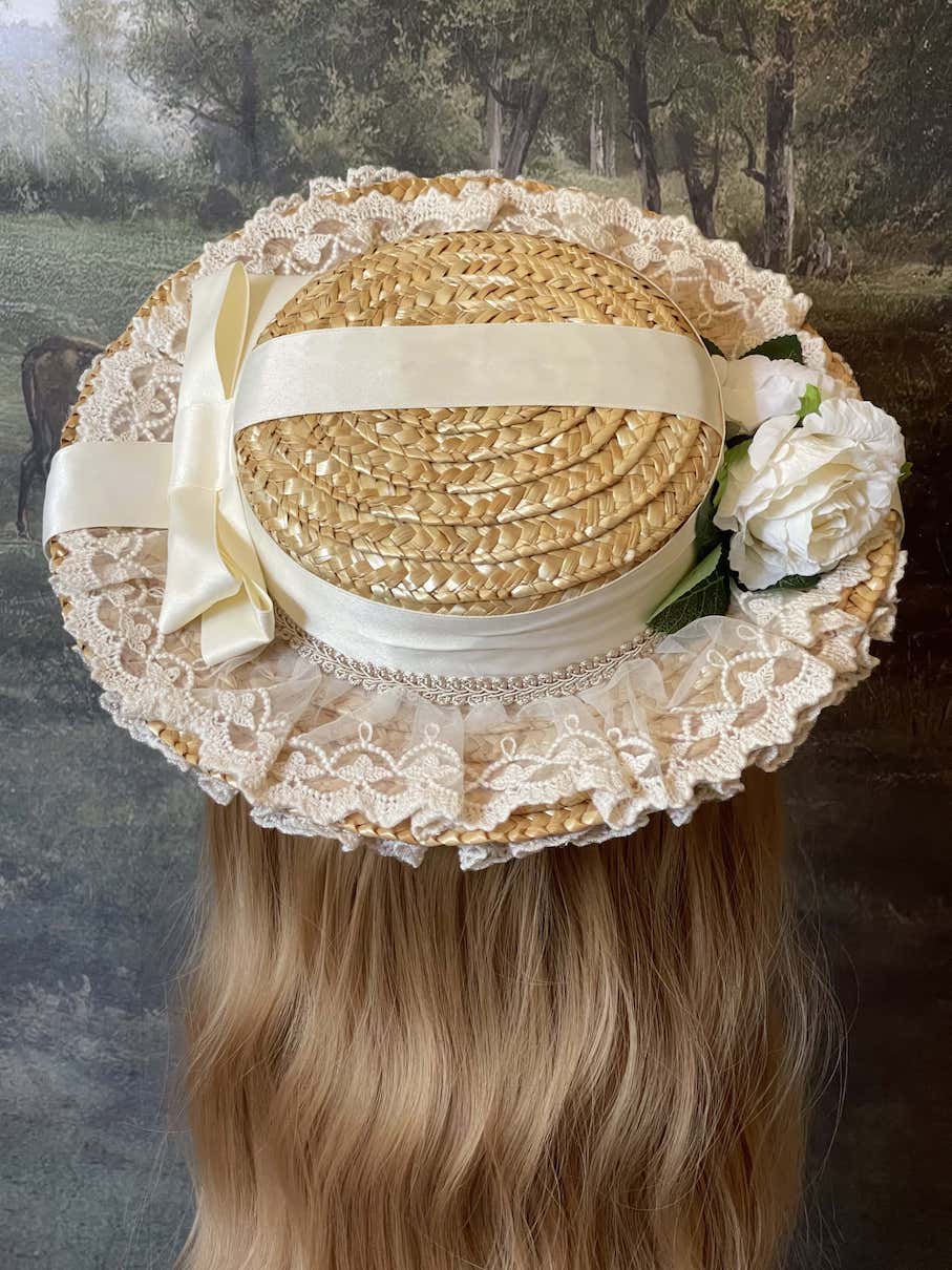 A historically inspired straw bonnet style hat with floral decorations, bow embellishments, ribbons, and lace.  Reminiscent of regency, rococo, victorian, and edwardian eras.