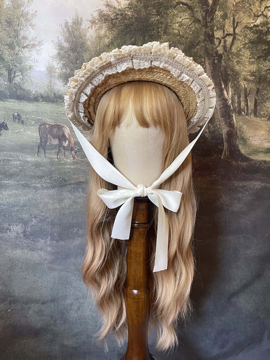 A historically inspired straw bonnet style hat with floral decorations, bow embellishments, ribbons, and lace.  Reminiscent of regency, rococo, victorian, and edwardian eras.