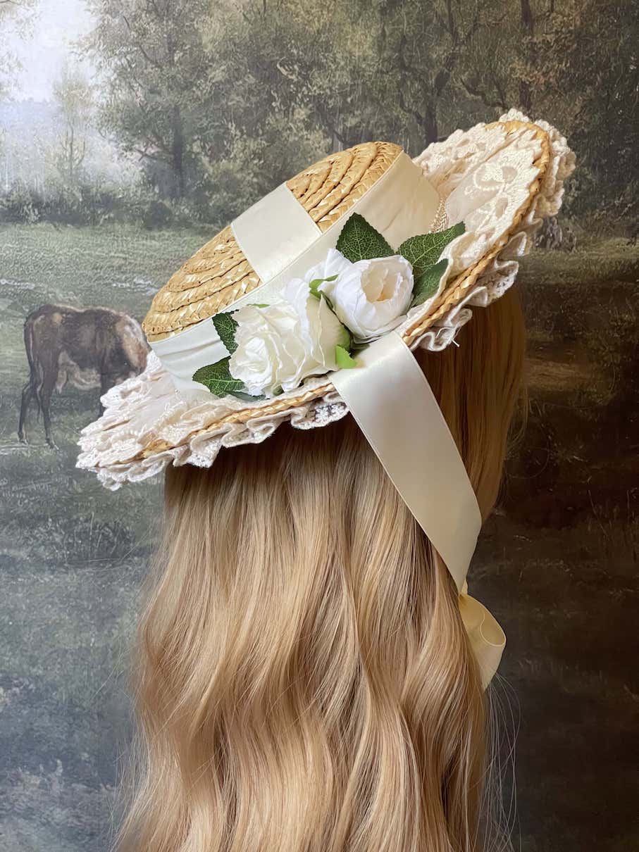 A historically inspired straw bonnet style hat with floral decorations, bow embellishments, ribbons, and lace.  Reminiscent of regency, rococo, victorian, and edwardian eras.