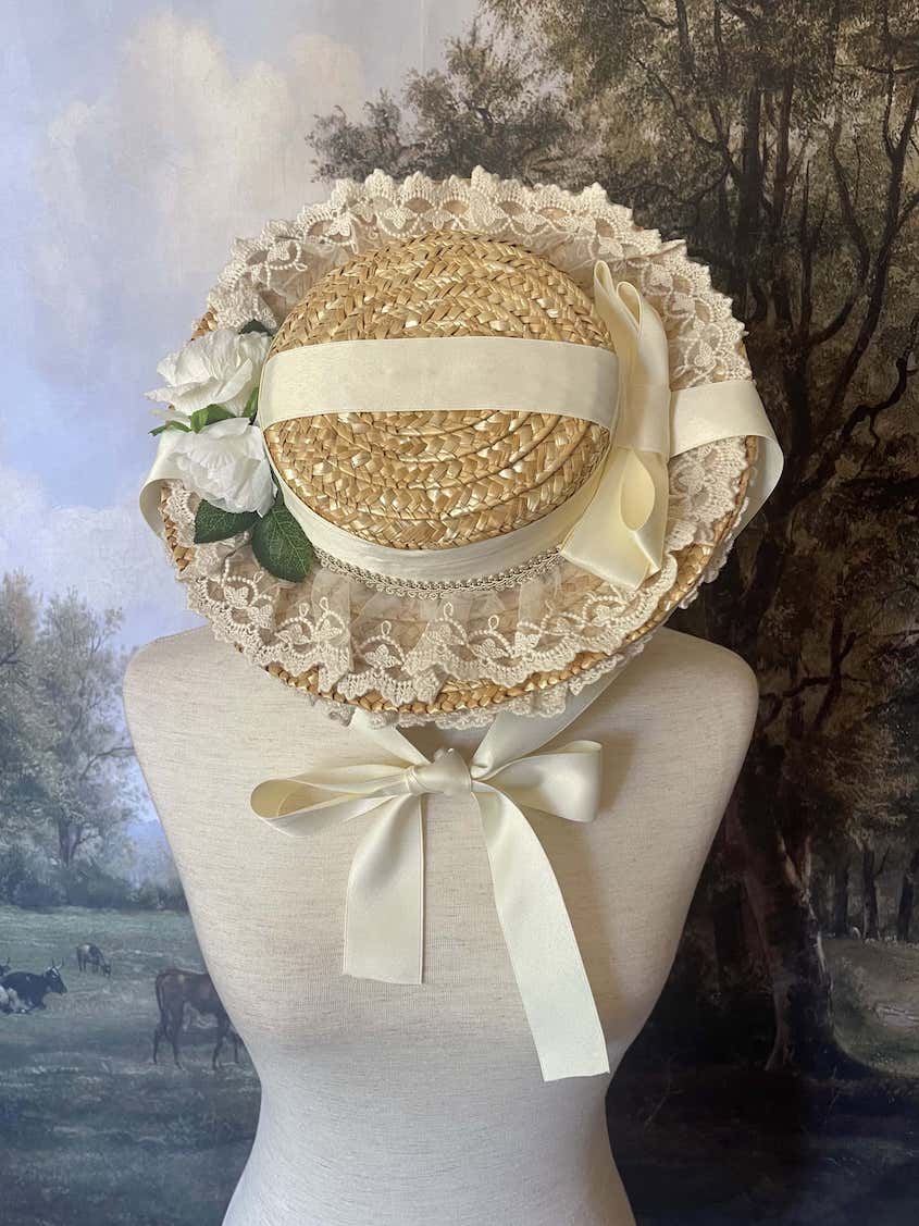 A historically inspired straw bonnet style hat with floral decorations, bow embellishments, ribbons, and lace.  Reminiscent of regency, rococo, victorian, and edwardian eras.