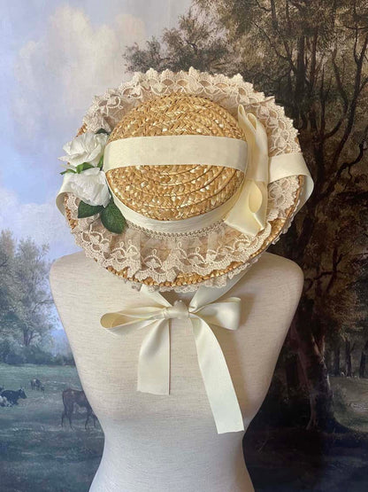 A historically inspired straw bonnet style hat with floral decorations, bow embellishments, ribbons, and lace.  Reminiscent of regency, rococo, victorian, and edwardian eras.