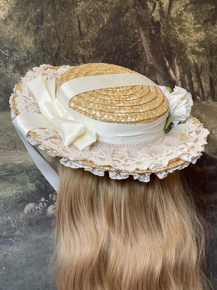 A historically inspired straw bonnet style hat with floral decorations, bow embellishments, ribbons, and lace.  Reminiscent of regency, rococo, victorian, and edwardian eras.