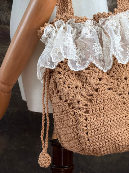 Vintage style crocheted bucket shoulder bag with lace trim on a mannequin against a scenic art history background
