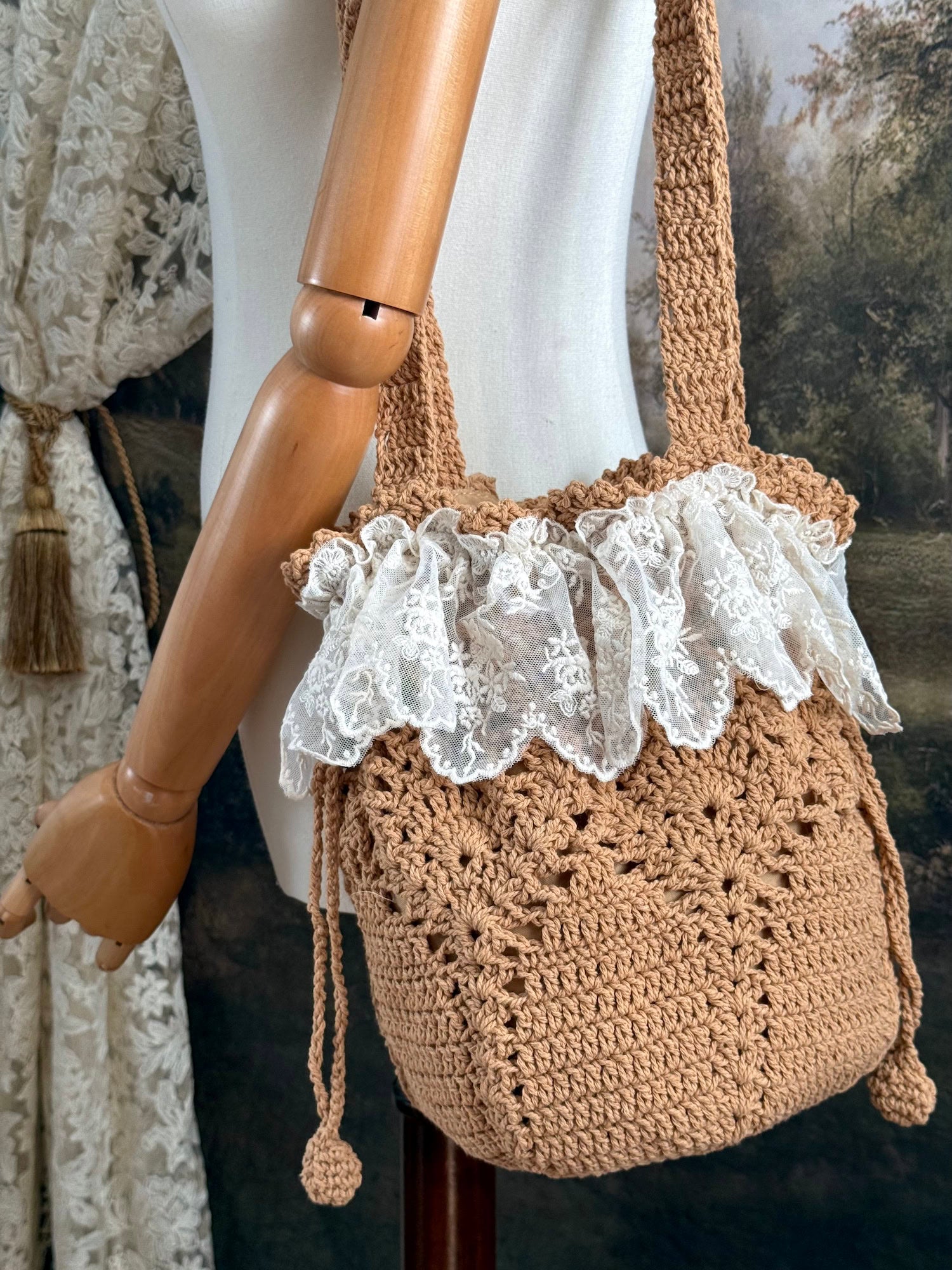 Vintage style crocheted bucket shoulder bag with lace trim on a mannequin against a scenic art history background