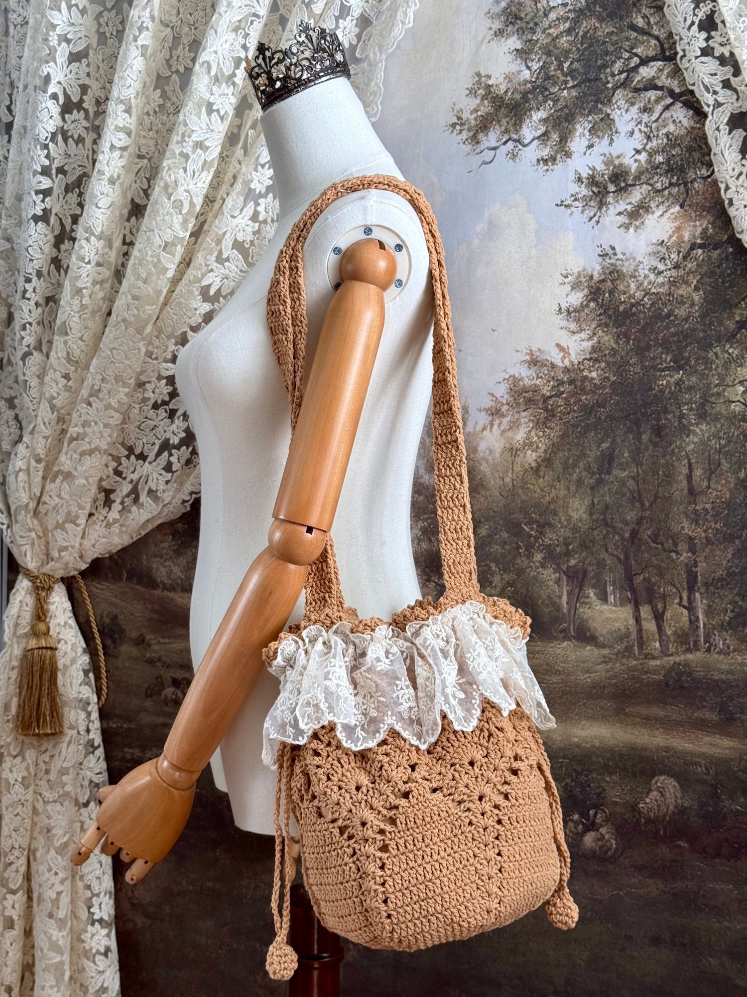 Vintage style crocheted bucket shoulder bag with lace trim on a mannequin against a scenic art history background