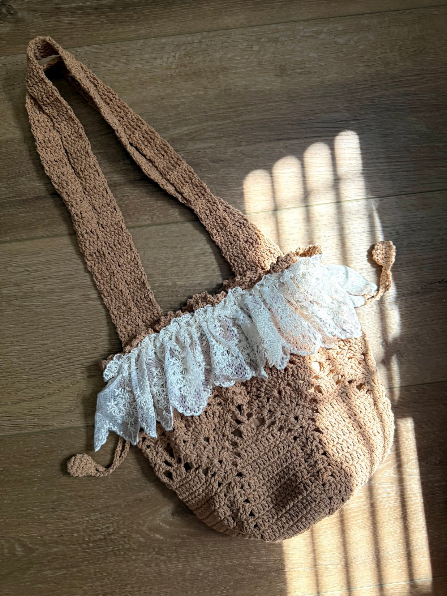 Vintage style crocheted bucket shoulder bag with lace trim against a wooden floor backdrop