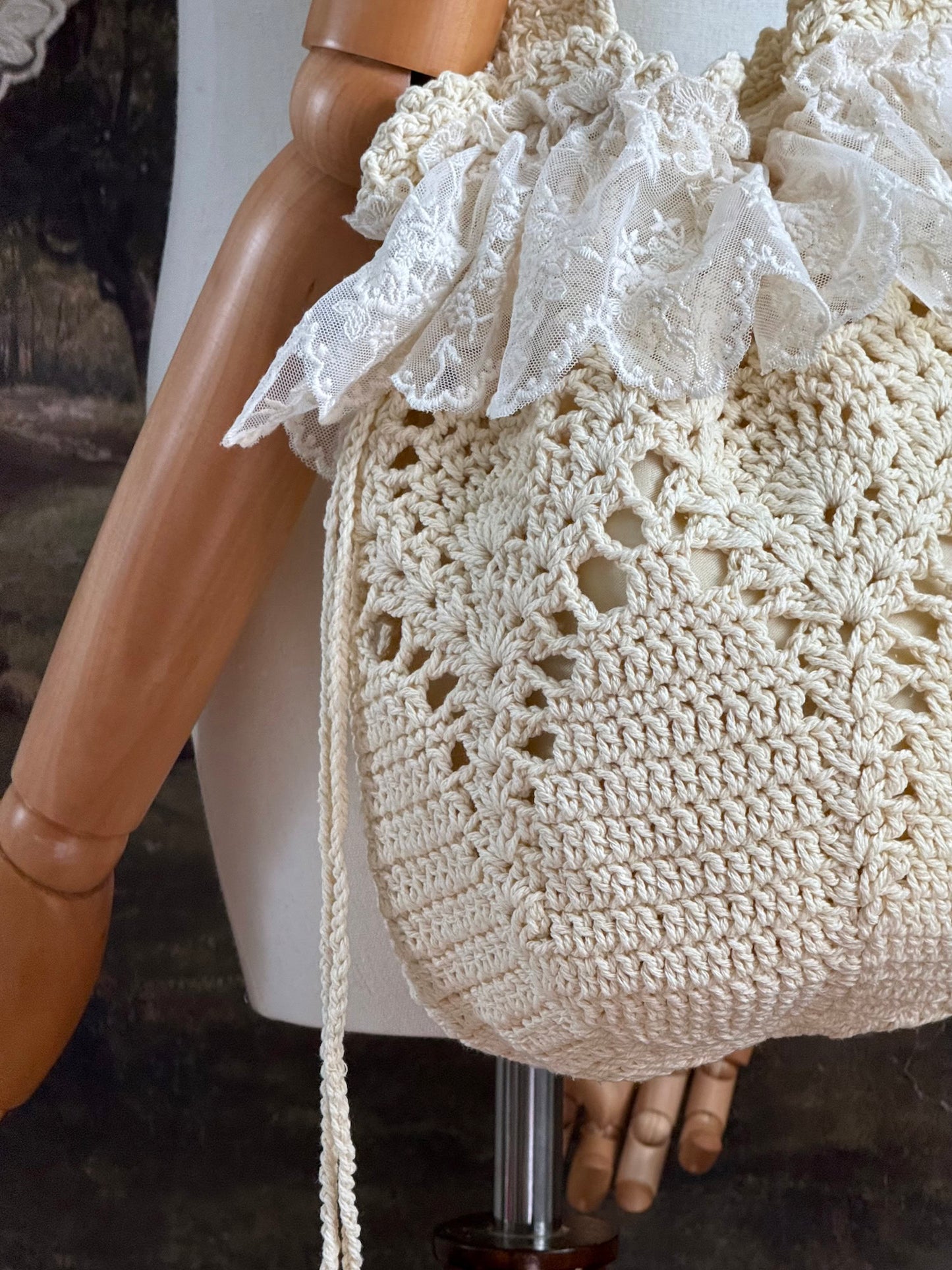 Vintage inspired crochet bucket shoulder bag with lace trim and drawstring closure, pictured on a mannequin in front of a historical painting backdrop.