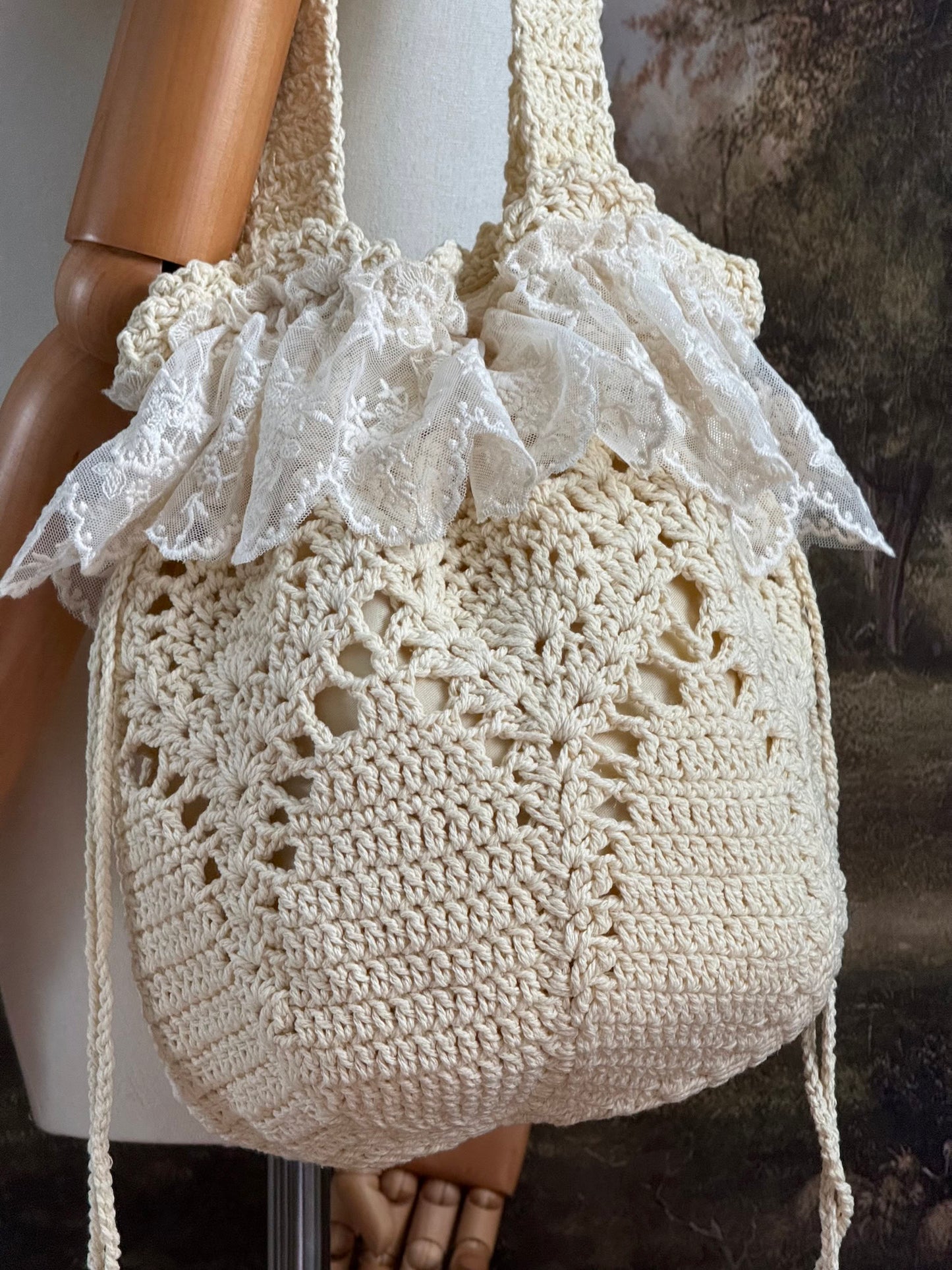 Vintage inspired crochet bucket shoulder bag with lace trim and drawstring closure, pictured on a mannequin in front of a historical painting backdrop.