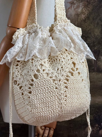 Vintage inspired crochet bucket shoulder bag with lace trim and drawstring closure, pictured on a mannequin in front of a historical painting backdrop.