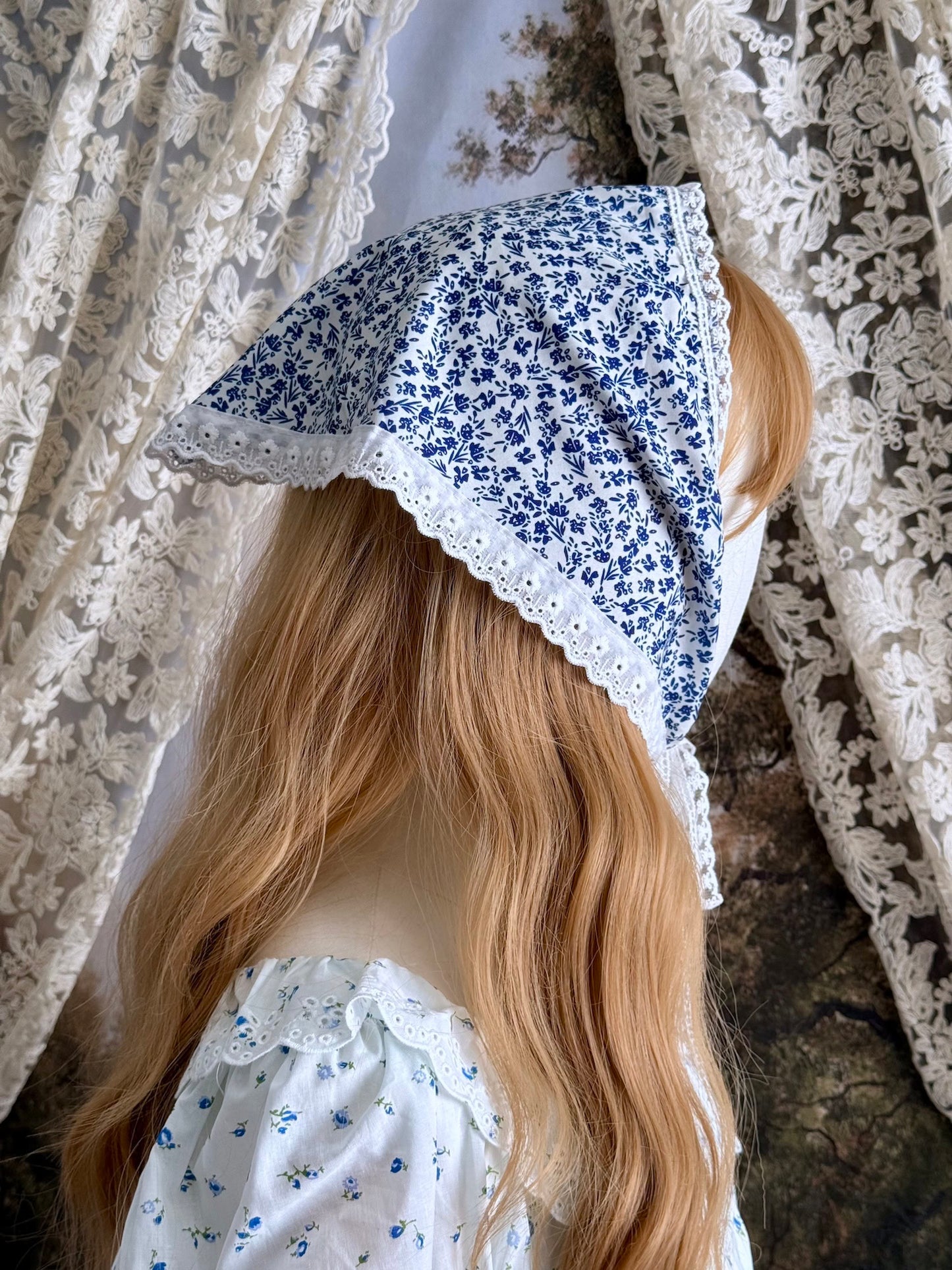 A vintage style historically inspired blue and white floral print babushka triangle headdress with floral lace trim pictured on a mannequin.