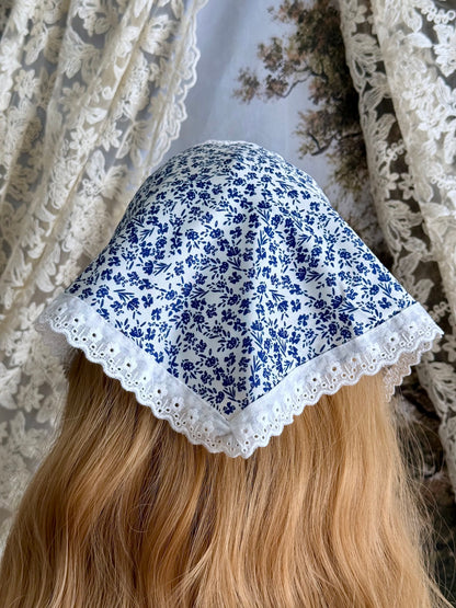 A vintage style historically inspired blue and white floral print babushka triangle headdress with floral lace trim pictured on a mannequin.