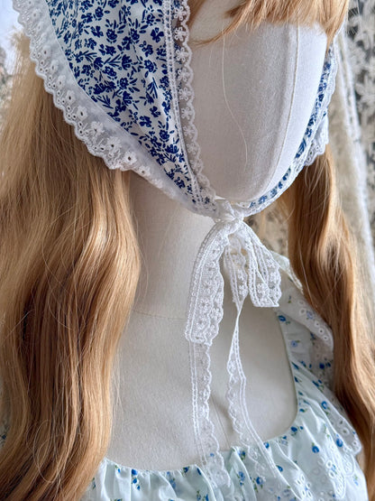 A vintage style historically inspired blue and white floral print babushka triangle headdress with floral lace trim pictured on a mannequin.