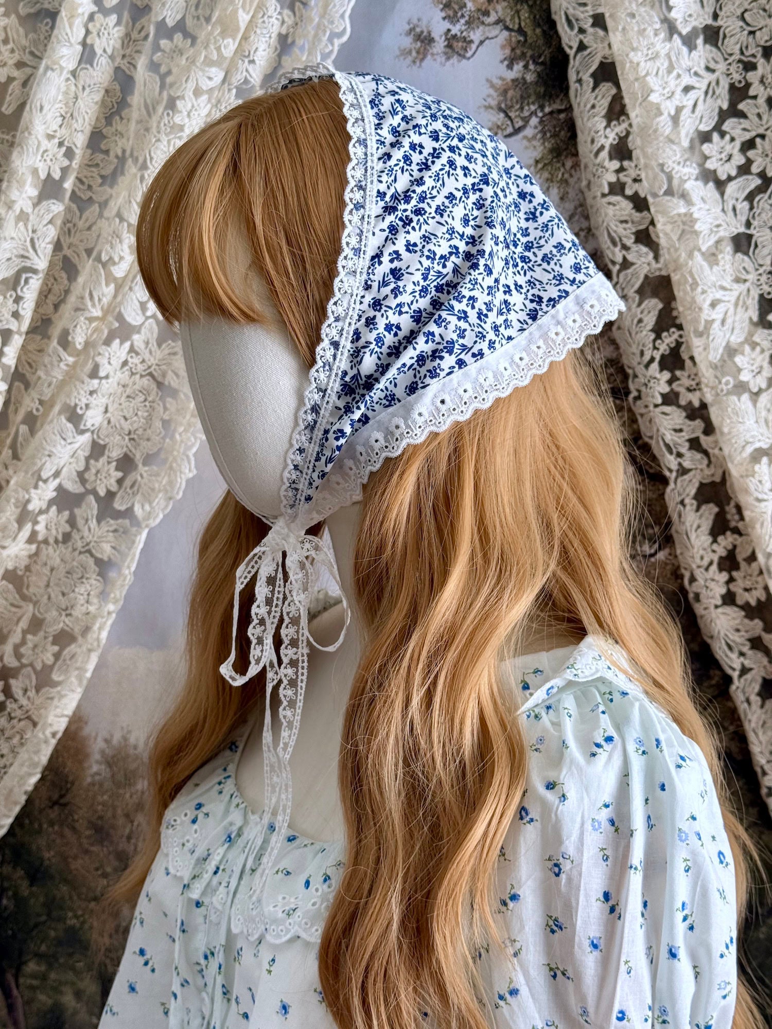 A vintage style historically inspired blue and white floral print babushka triangle headdress with floral lace trim pictured on a mannequin.