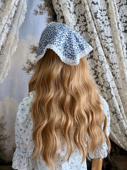 A vintage style historically inspired blue and white floral print babushka triangle headdress with floral lace trim pictured on a mannequin.