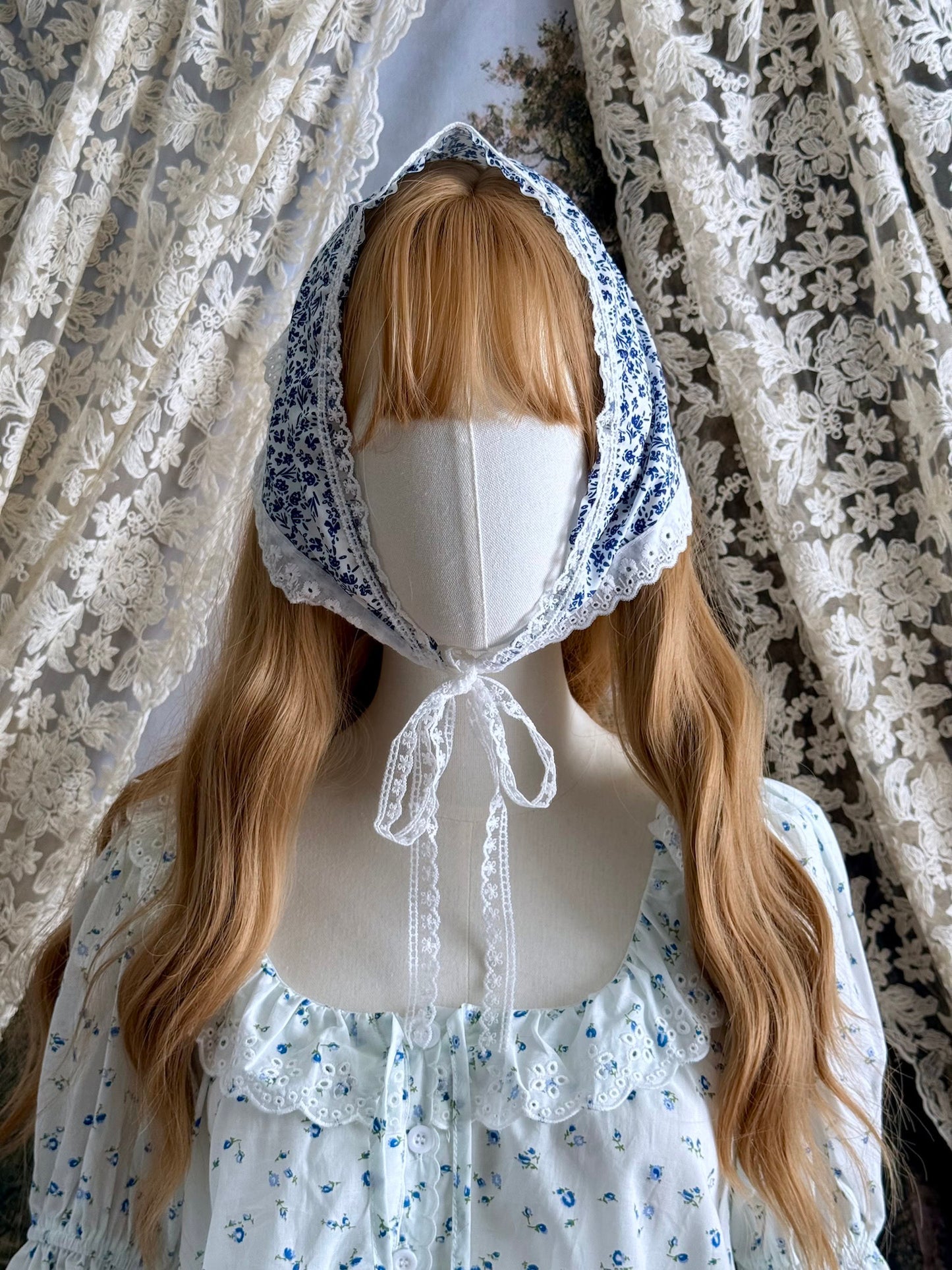 A vintage style historically inspired blue and white floral print babushka triangle headdress with floral lace trim pictured on a mannequin.