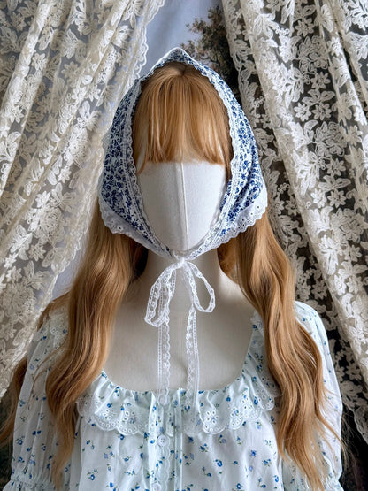 A vintage style historically inspired blue and white floral print babushka triangle headdress with floral lace trim pictured on a mannequin.