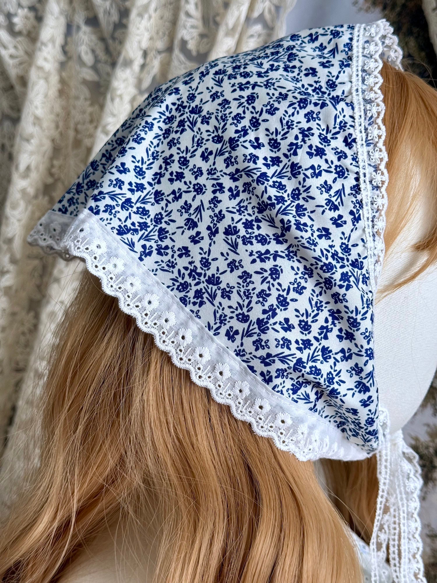 A vintage style historically inspired blue and white floral print babushka triangle headdress with floral lace trim pictured on a mannequin.