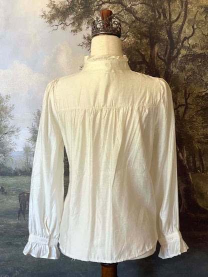 A historically inspired victorian and edwardian era style ivory colored blouse with pintucks, a high neck collar, ruffle hem sleeves, and crochet lace.