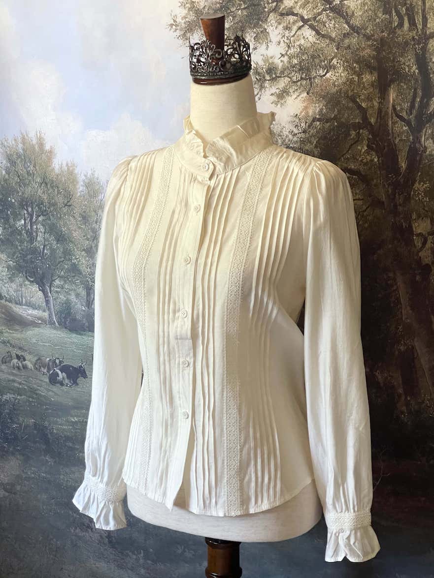 A historically inspired victorian and edwardian era style ivory colored blouse with pintucks, a high neck collar, ruffle hem sleeves, and crochet lace.