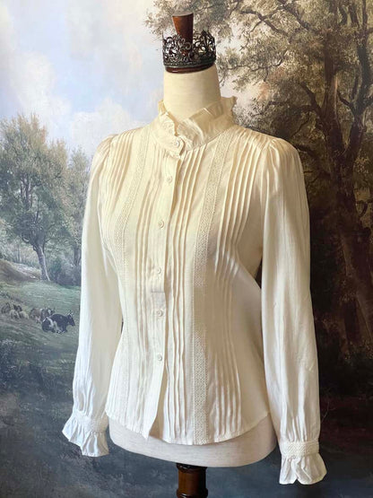 A historically inspired victorian and edwardian era style ivory colored blouse with pintucks, a high neck collar, ruffle hem sleeves, and crochet lace.
