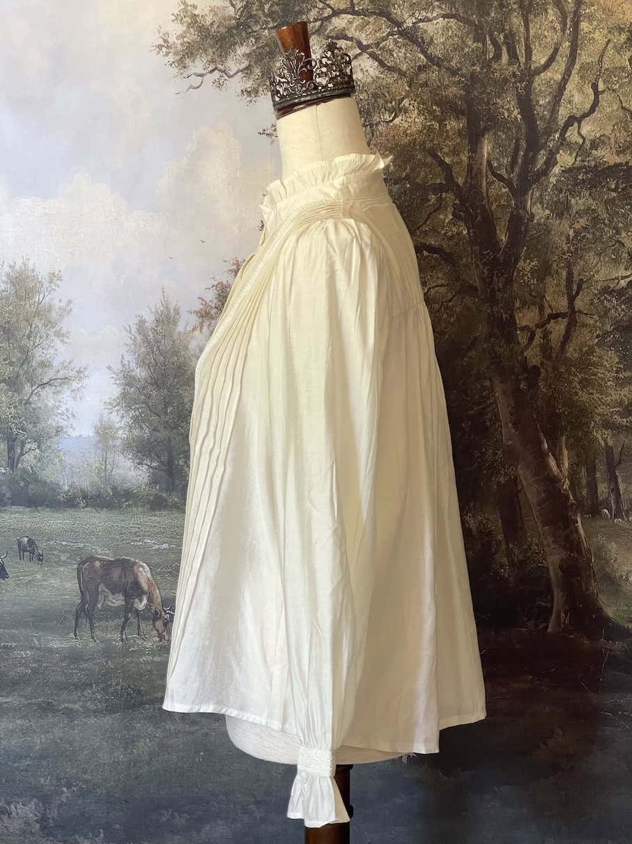 A historically inspired victorian and edwardian era style ivory colored blouse with pintucks, a high neck collar, ruffle hem sleeves, and crochet lace.