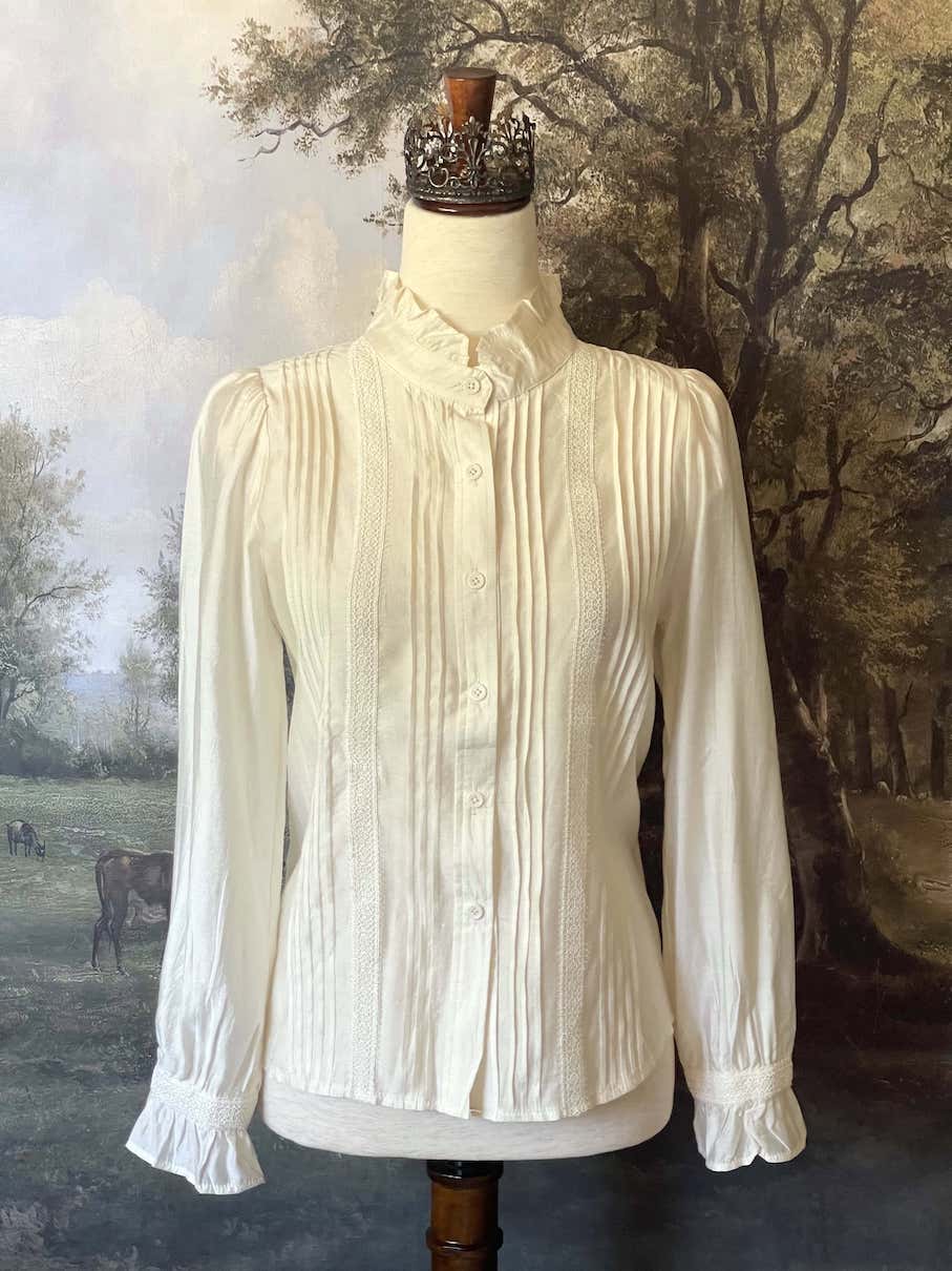 A historically inspired victorian and edwardian era style ivory colored blouse with pintucks, a high neck collar, ruffle hem sleeves, and crochet lace.