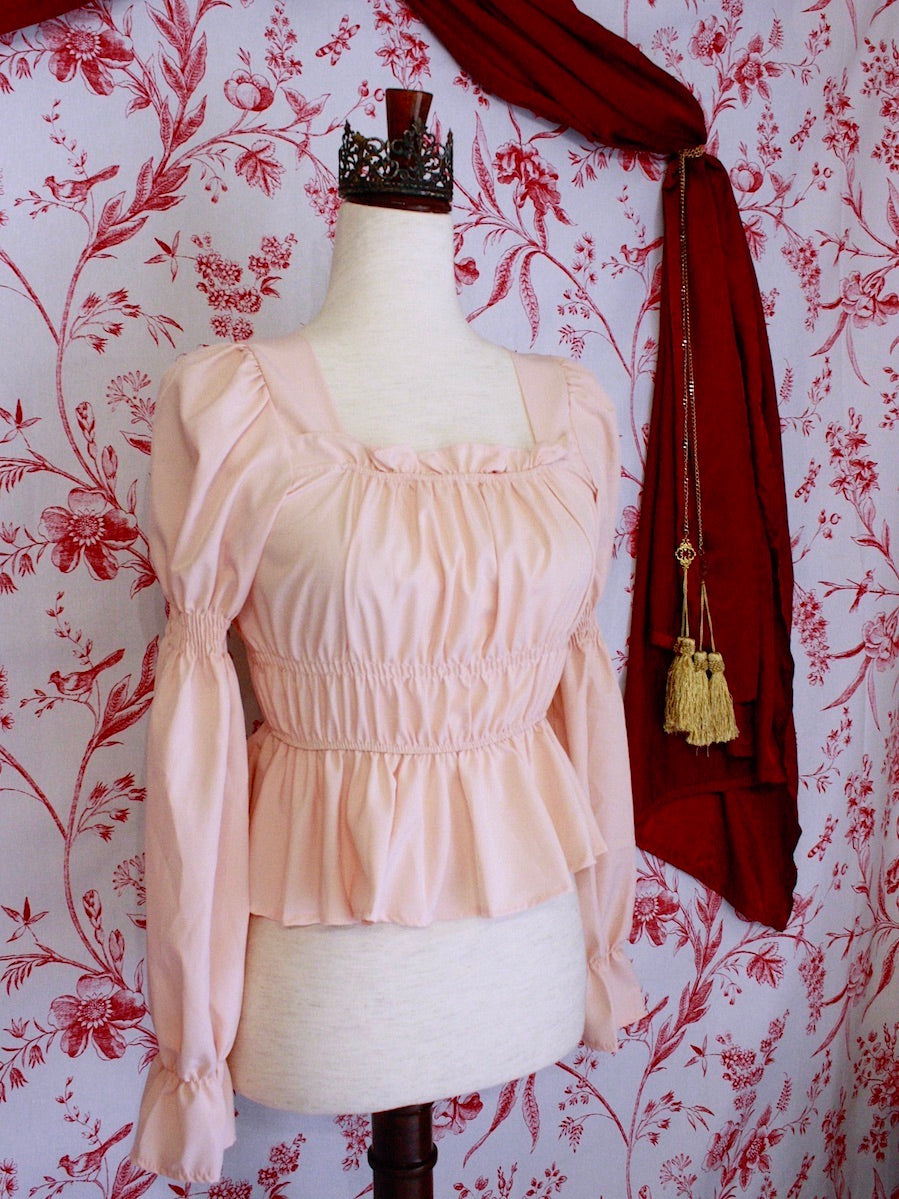 Historically Inspired Renaissance Smocked Blouse with Juliet Puff Sleeves in Peachy Pink, in front of a toile backdrop.
